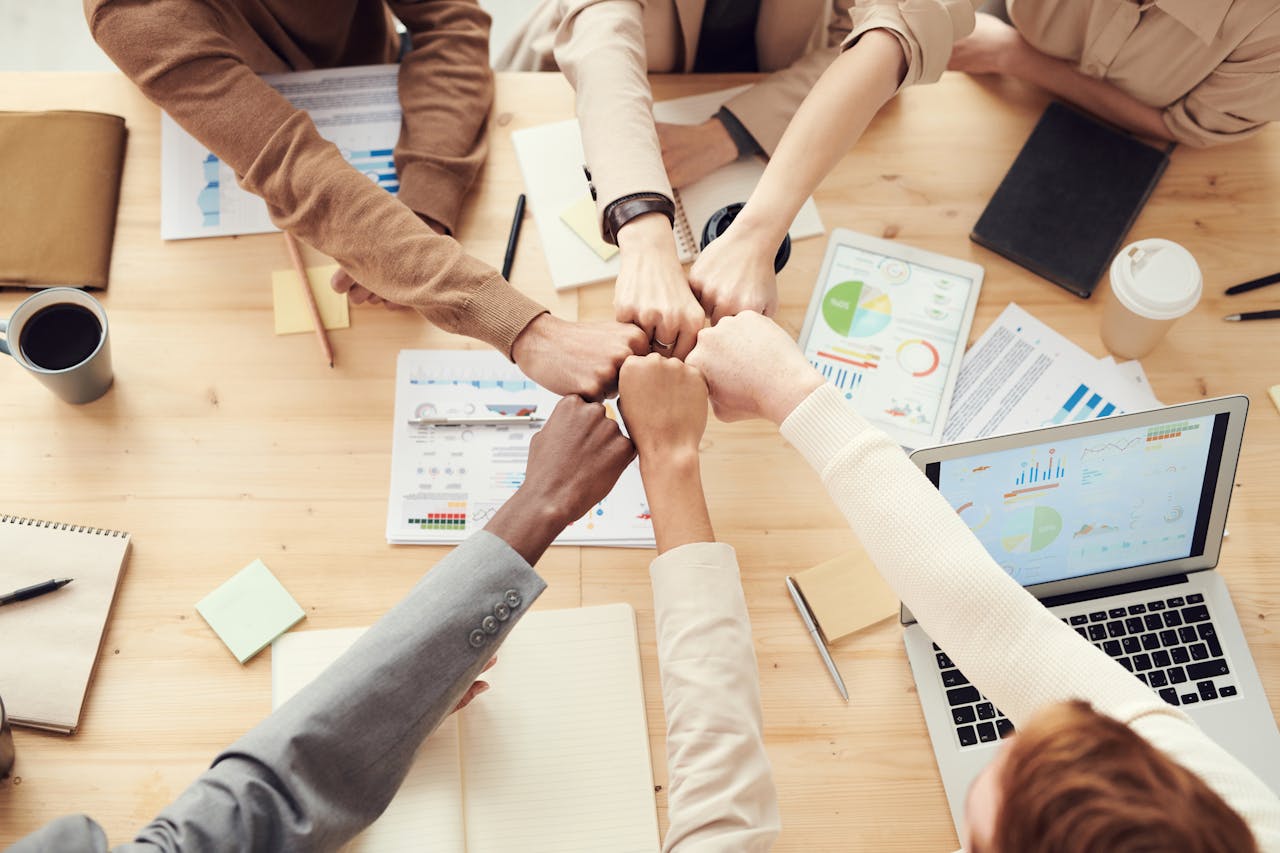 digital Top view of a diverse team fist bumping over a meeting table with paperwork and laptops, symbolizing teamwork.